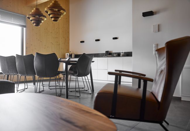 Woonkamer Alm Lodge 4 Woonkamer met fauteuil en keuken op de achtergrond in Alm Logde 4